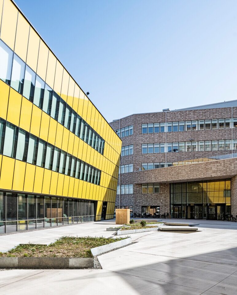 Yellow glass facade of Linnaeus University next to a brick building and a paved courtyard